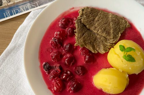 Wołowina w sosie wiśniowym - przepis na soczyste mięso w aromatycznym, słodko-kwaśnym sosie wiśniowym, podane elegancko na talerzu z ziołami i świeżymi wiśniami.